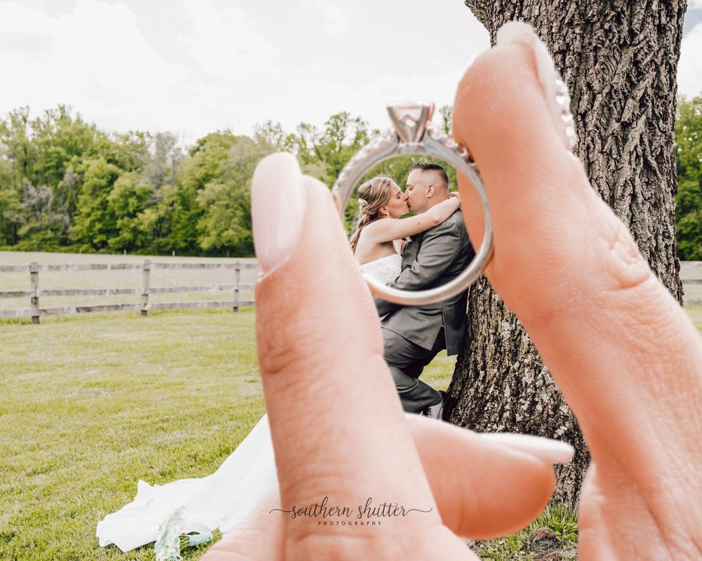 Creative outdoor photo framed through fingers showing silhouettes relaxing under a tree in a grassy field.