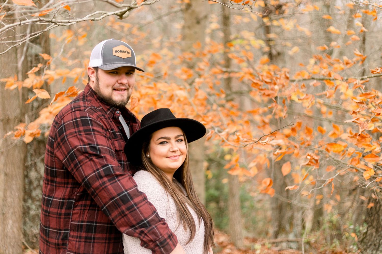 A couple embraces under orange autumn leaves in a romantic outdoor setting.