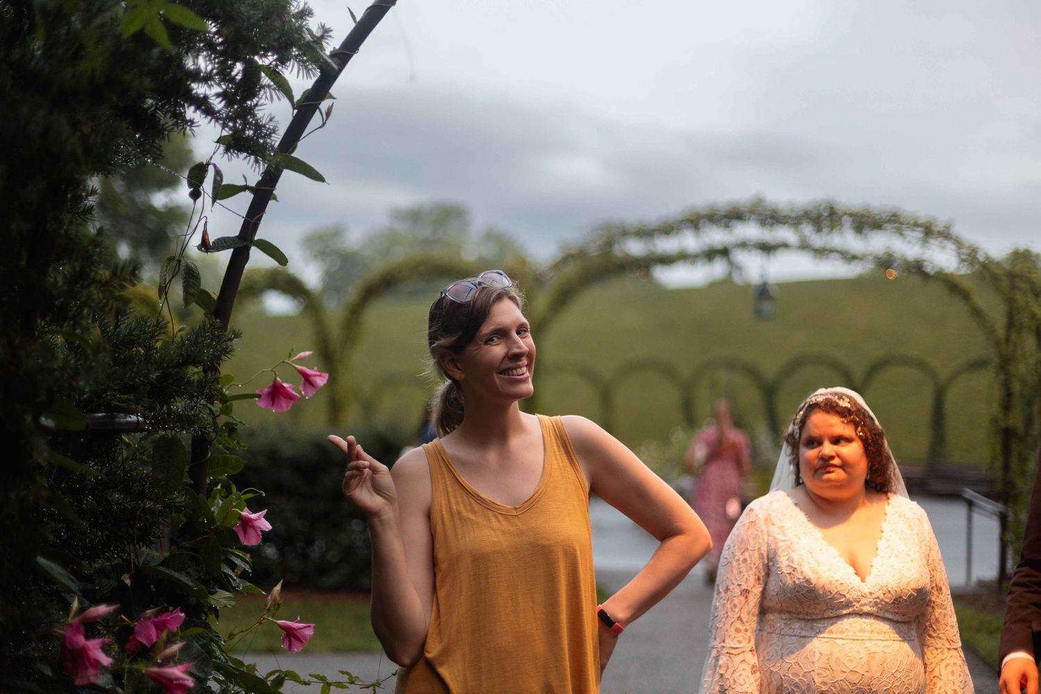 Two people share a laugh in garden setting with pink flowers and archway.