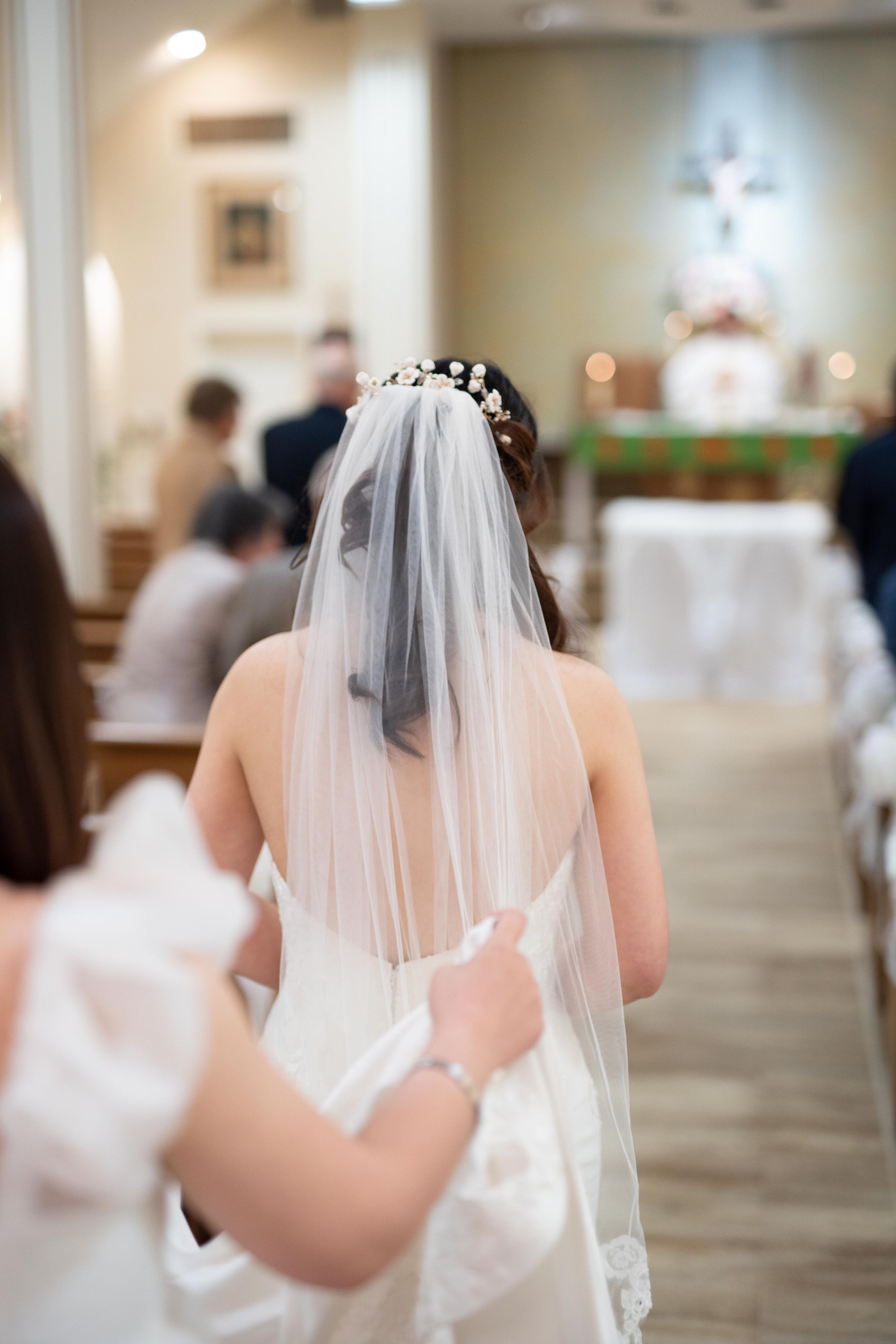 Back view of bride in white dress with flowing veil in church setting.