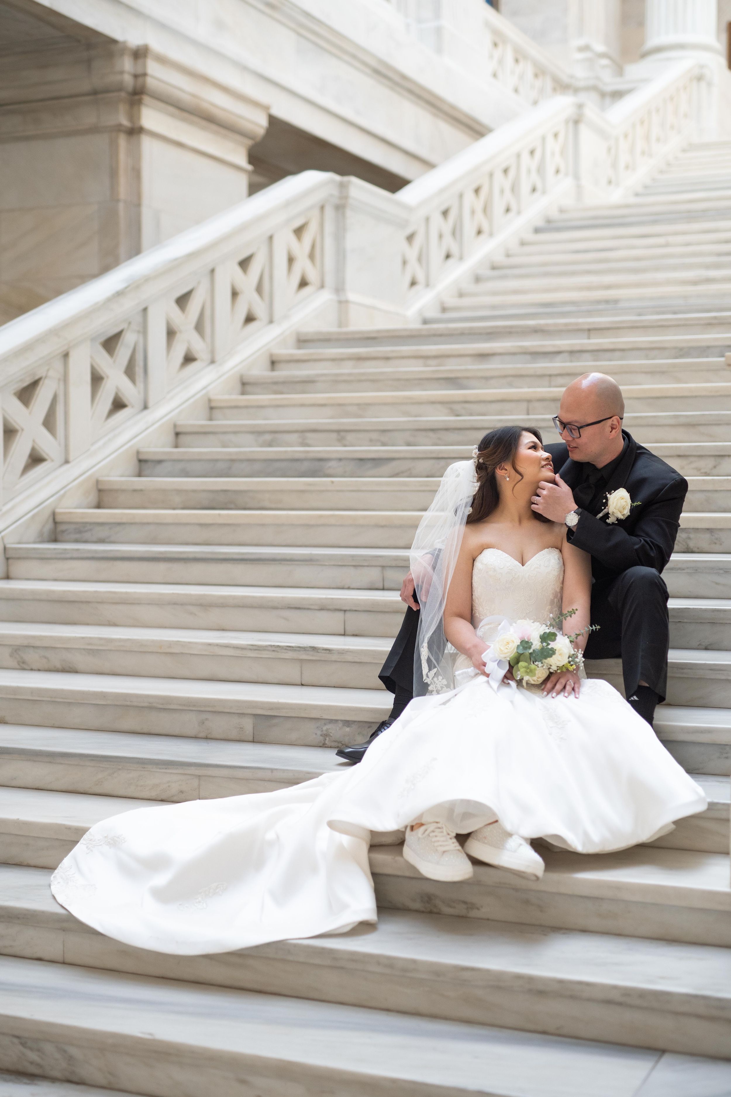 Newlyweds sitting together on grand white marble steps.
