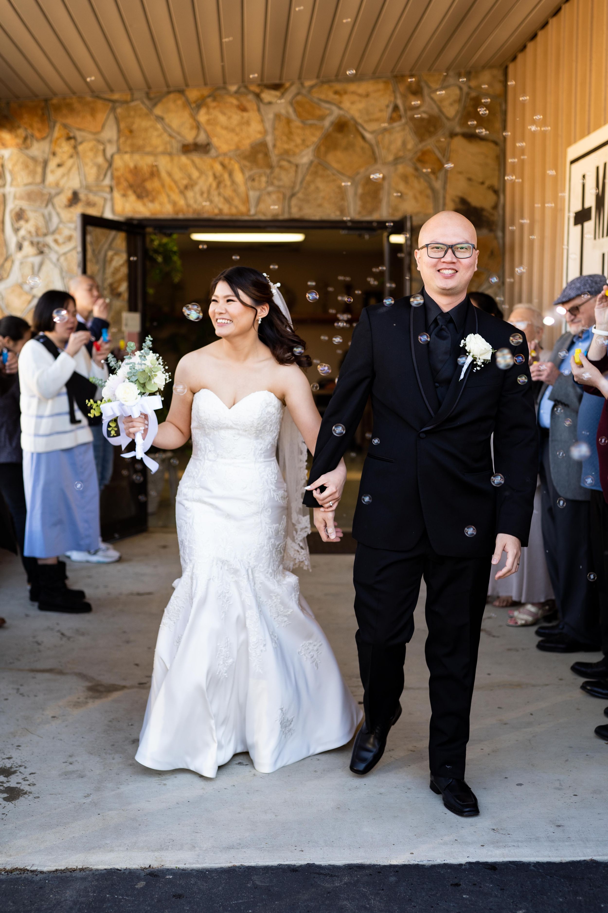 Wedding couple walking through stone archway surrounded by guests.