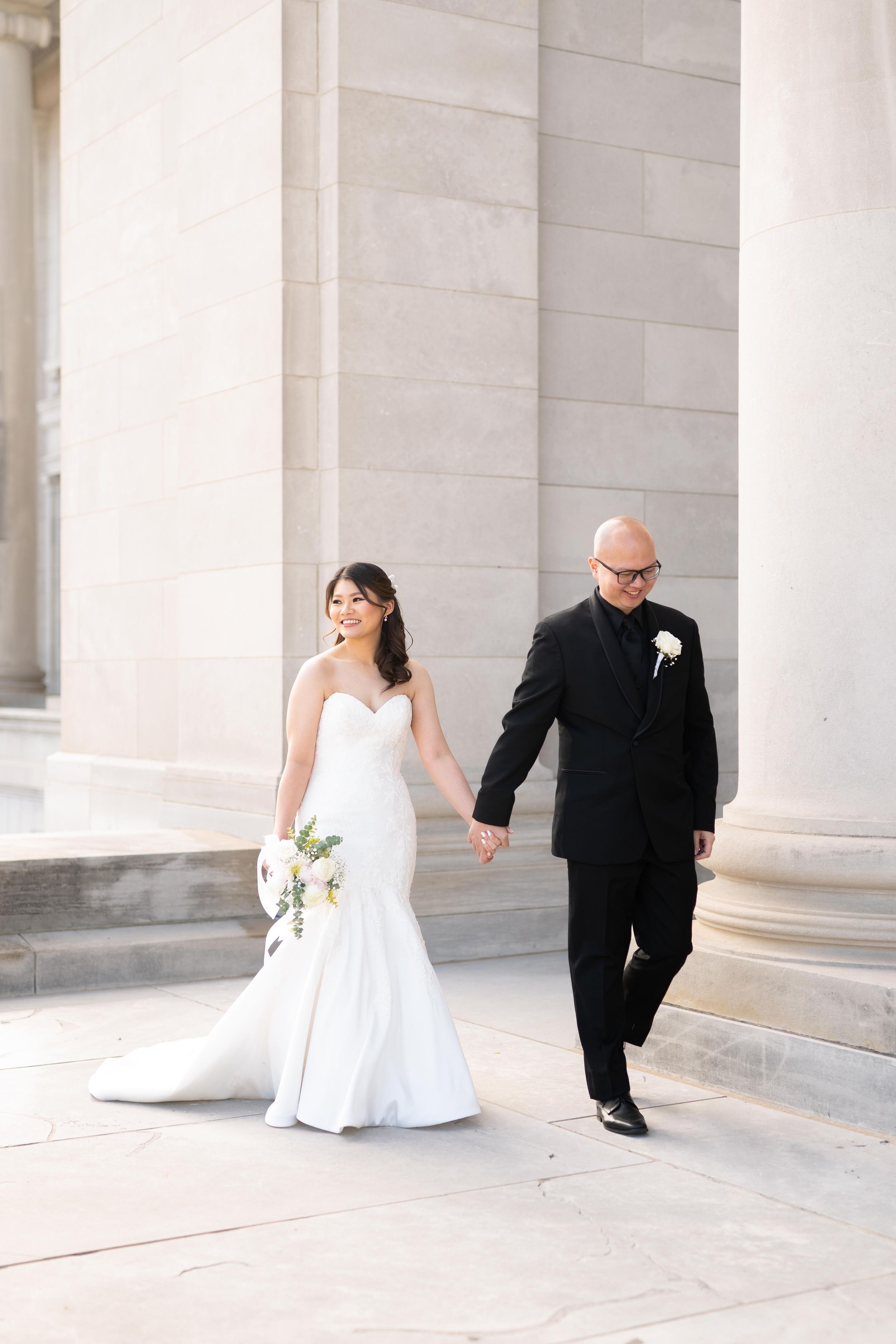 Wedding couple walking hand in hand through elegant marble columns.