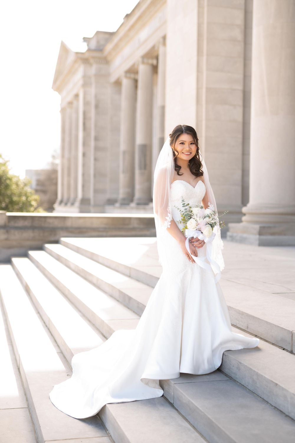 Bride in classic white gown posed on grand stone steps with columns.