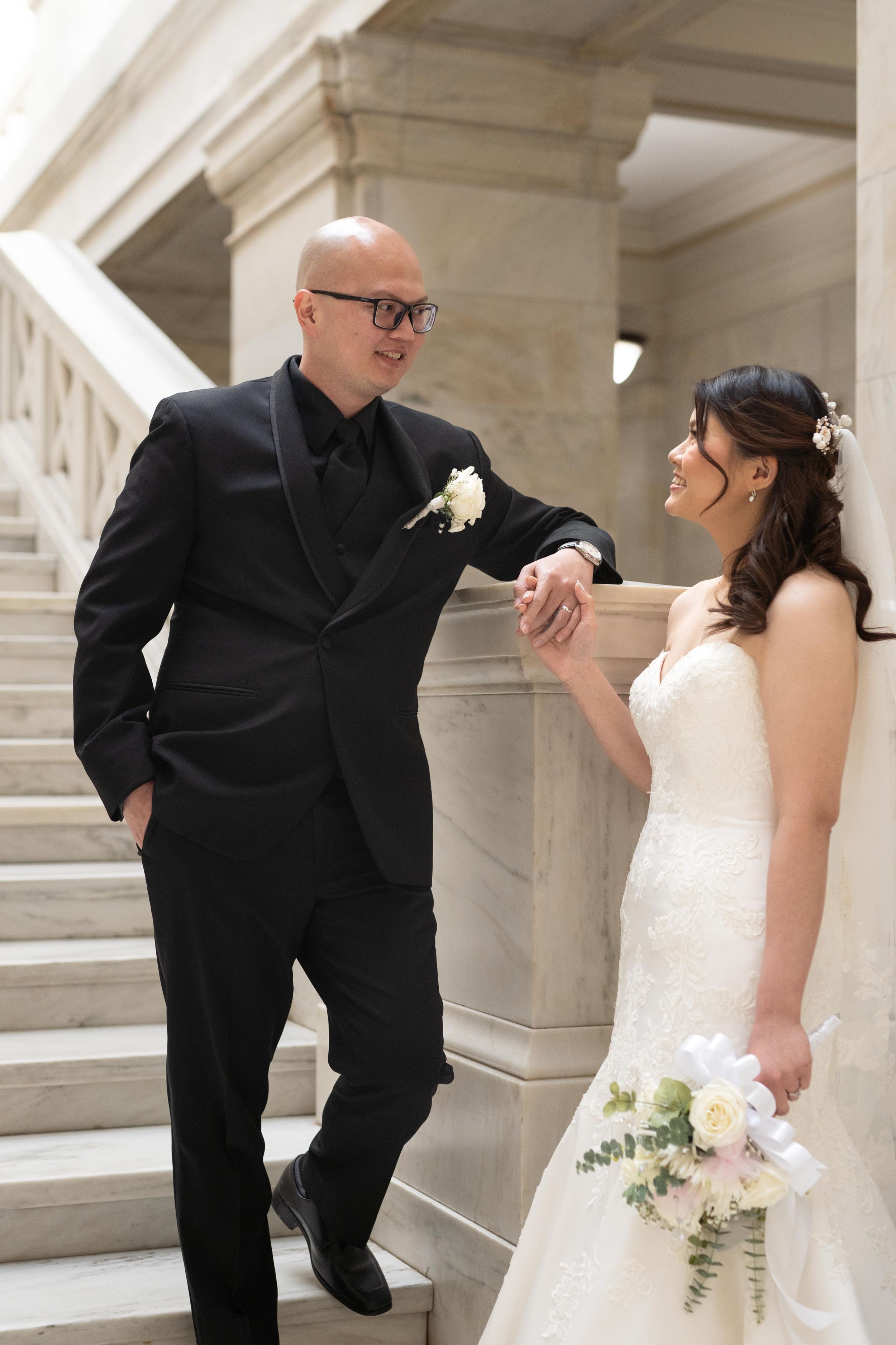 Joyful couple sharing playful moment on marble staircase at wedding.