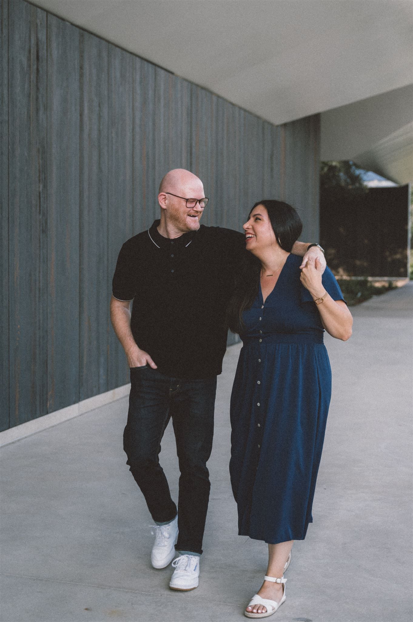 A couple laughs together while walking along a modern building corridor.