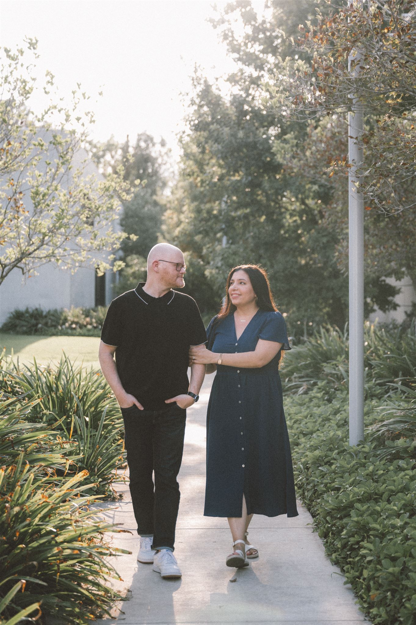 A couple takes a romantic stroll along a landscaped pathway during golden hour.