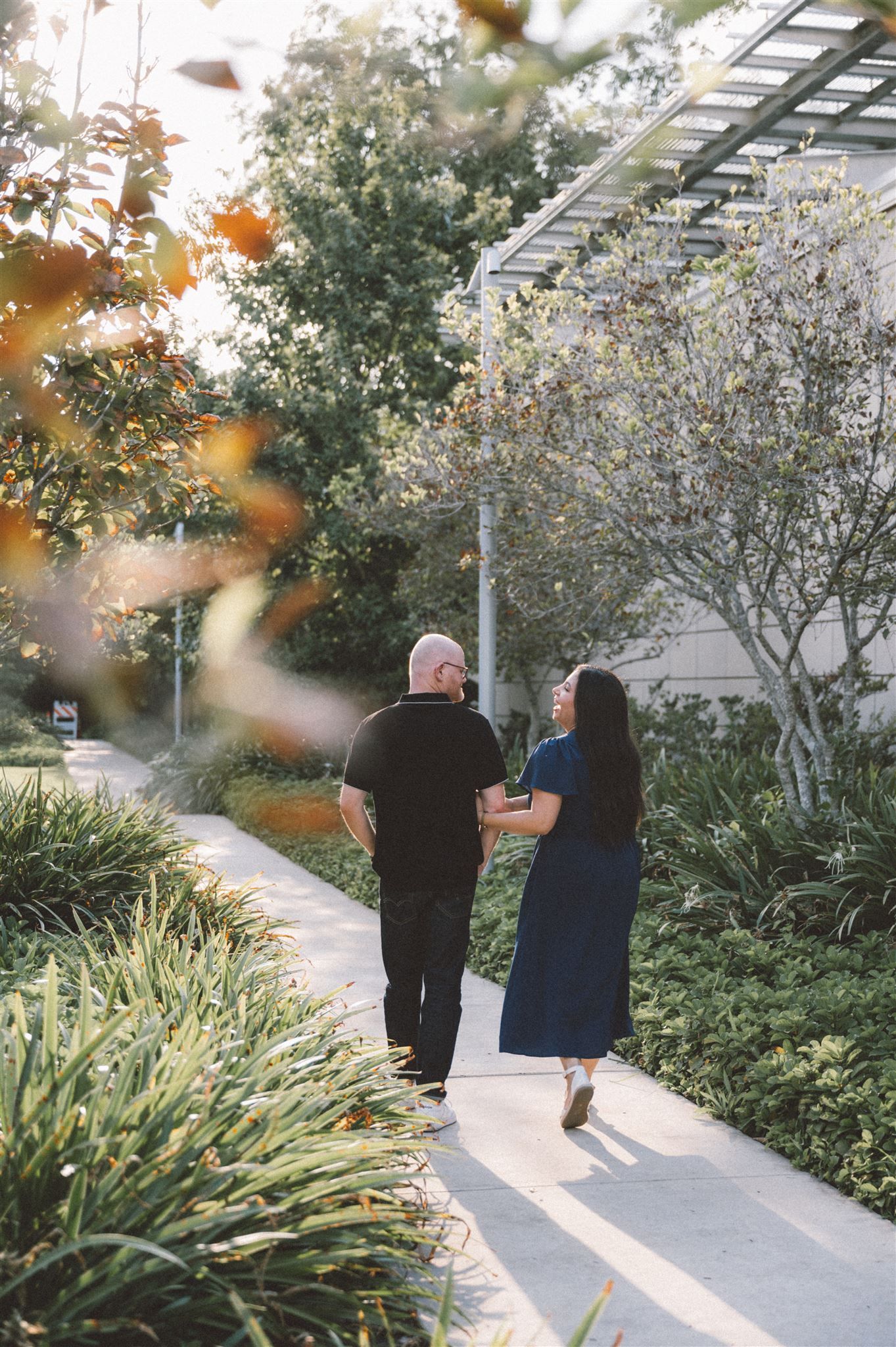 A couple walks hand in hand along a garden path on a sunny afternoon.