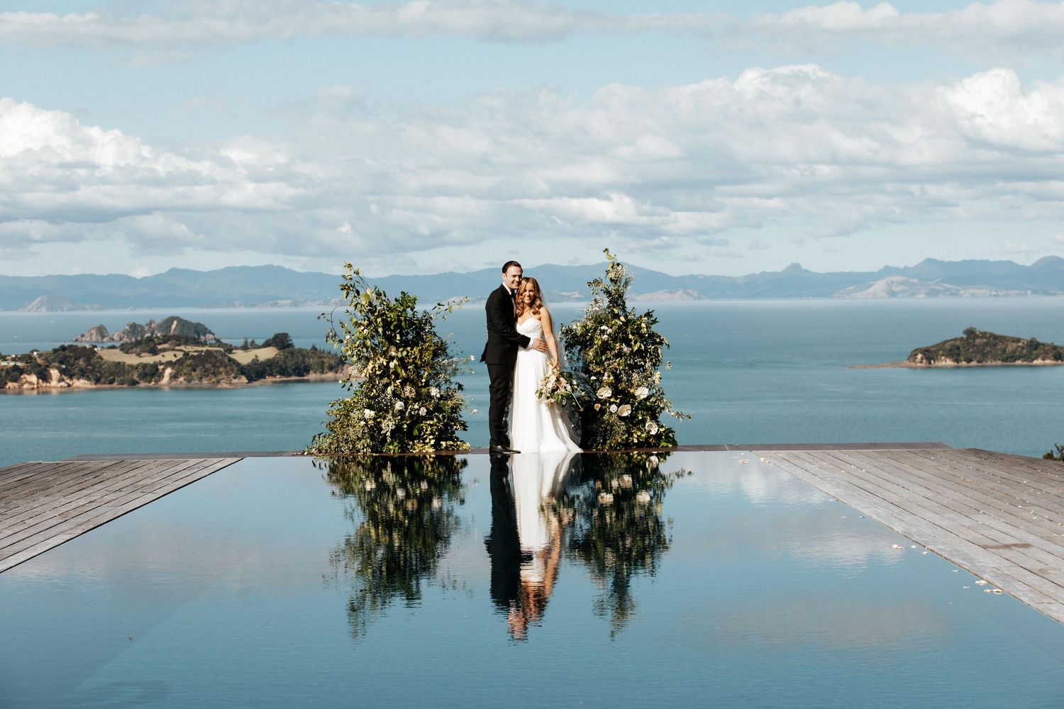 Wedding ceremony setup with floral arrangements reflected in infinity pool overlooking mountain vista.