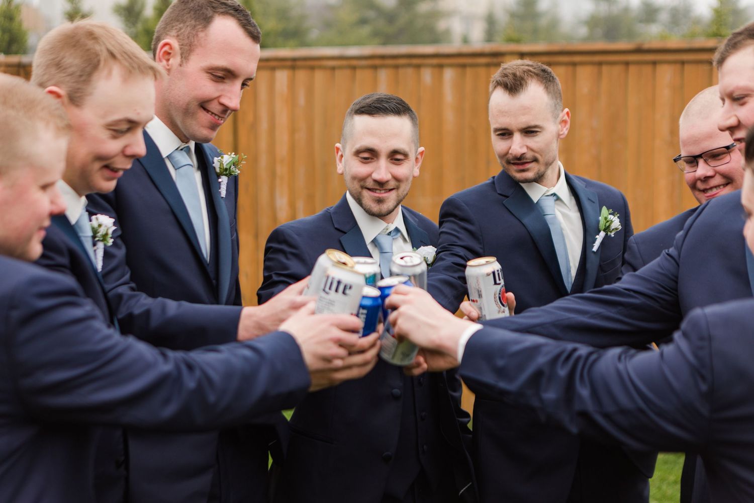 Groomsmen in navy suits toast with drinks in an outdoor celebration.