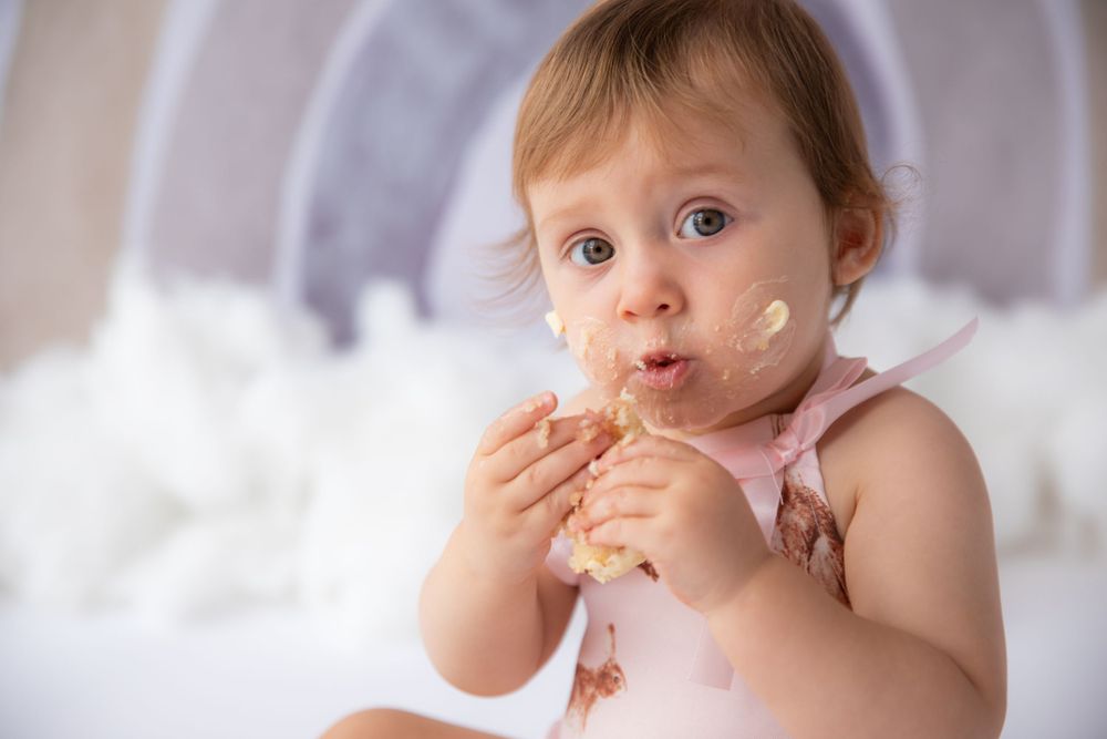 Baby with messy face enjoying snack against pastel rainbow background.