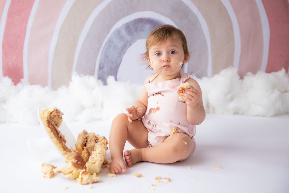 Baby sitting against pastel rainbow backdrop with clouds and cookie crumbs.