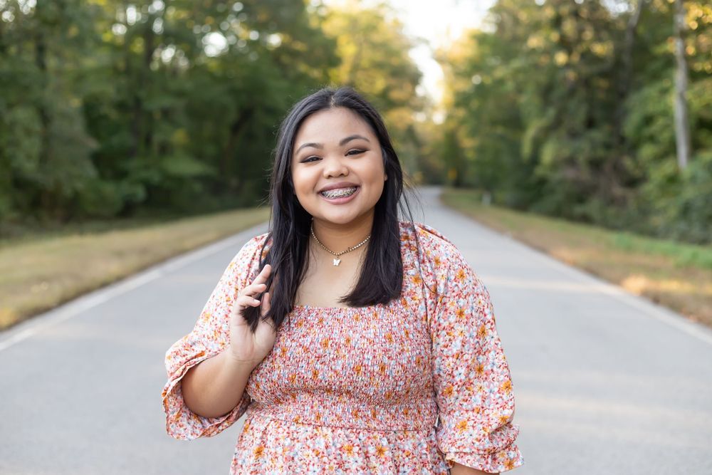 Person wearing a pink floral dress poses on a tree-lined road during golden hour.