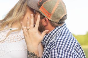 A close-up engagement moment between couple in casual attire with focus on ring hand.
