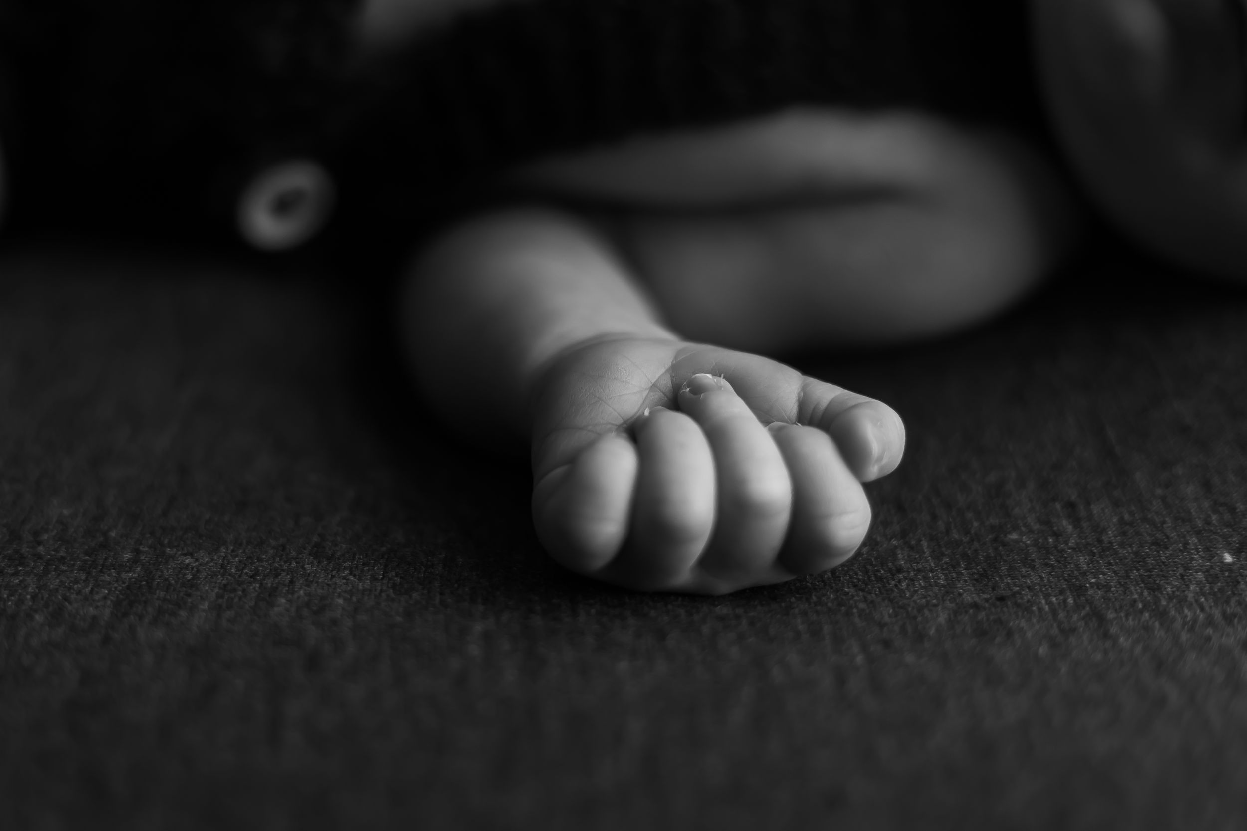Close-up black and white photo of a tiny baby's hand resting on textured surface.