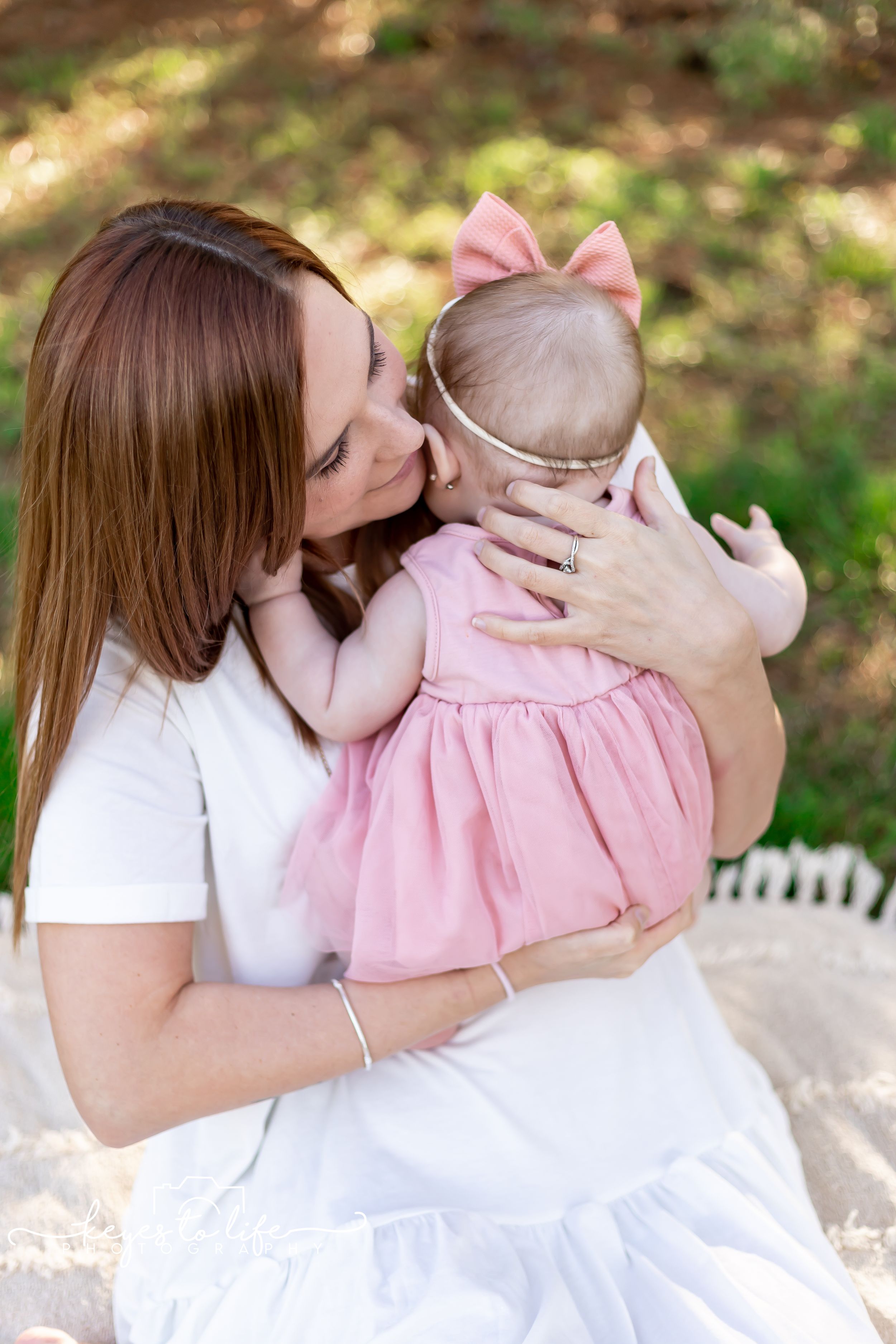 Tender moment between parent and baby in pink dress outdoors.