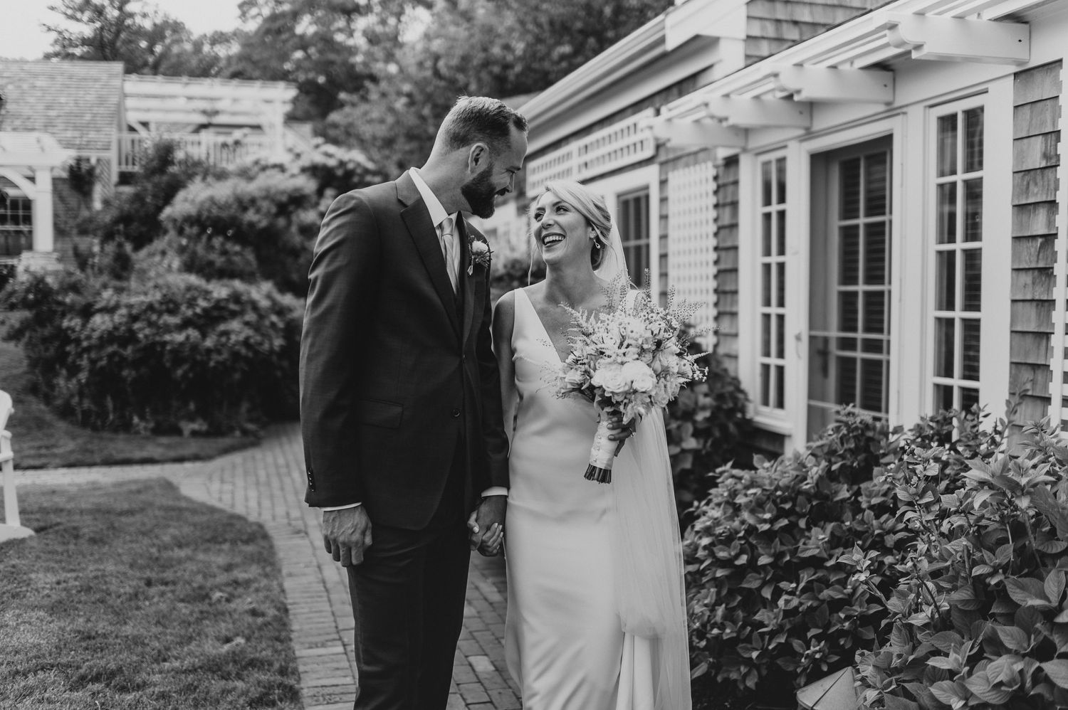A candid black and white wedding moment captured in front of a classic white building with lattice details.