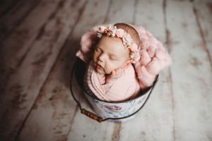 Artistic overhead shot of sleeping newborn in pink wrap on vintage-style bowl.
