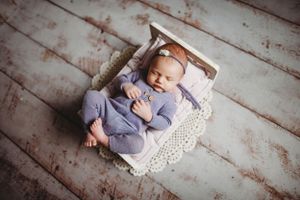 Peaceful newborn sleeping on white lace blanket with soft gray outfit.