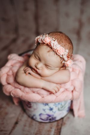 Delicate newborn portrait in floral bowl with pink wrap and soft lighting.