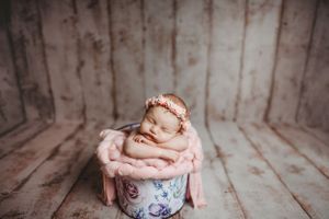 Artistic newborn photography with vintage floral bowl and rustic wooden background.
