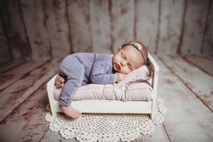 Professional newborn portrait in soft gray outfit on white lace blanket.