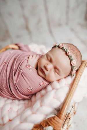 Dreamy newborn photography featuring mauve wrap and delicate crown on rustic wooden backdrop.