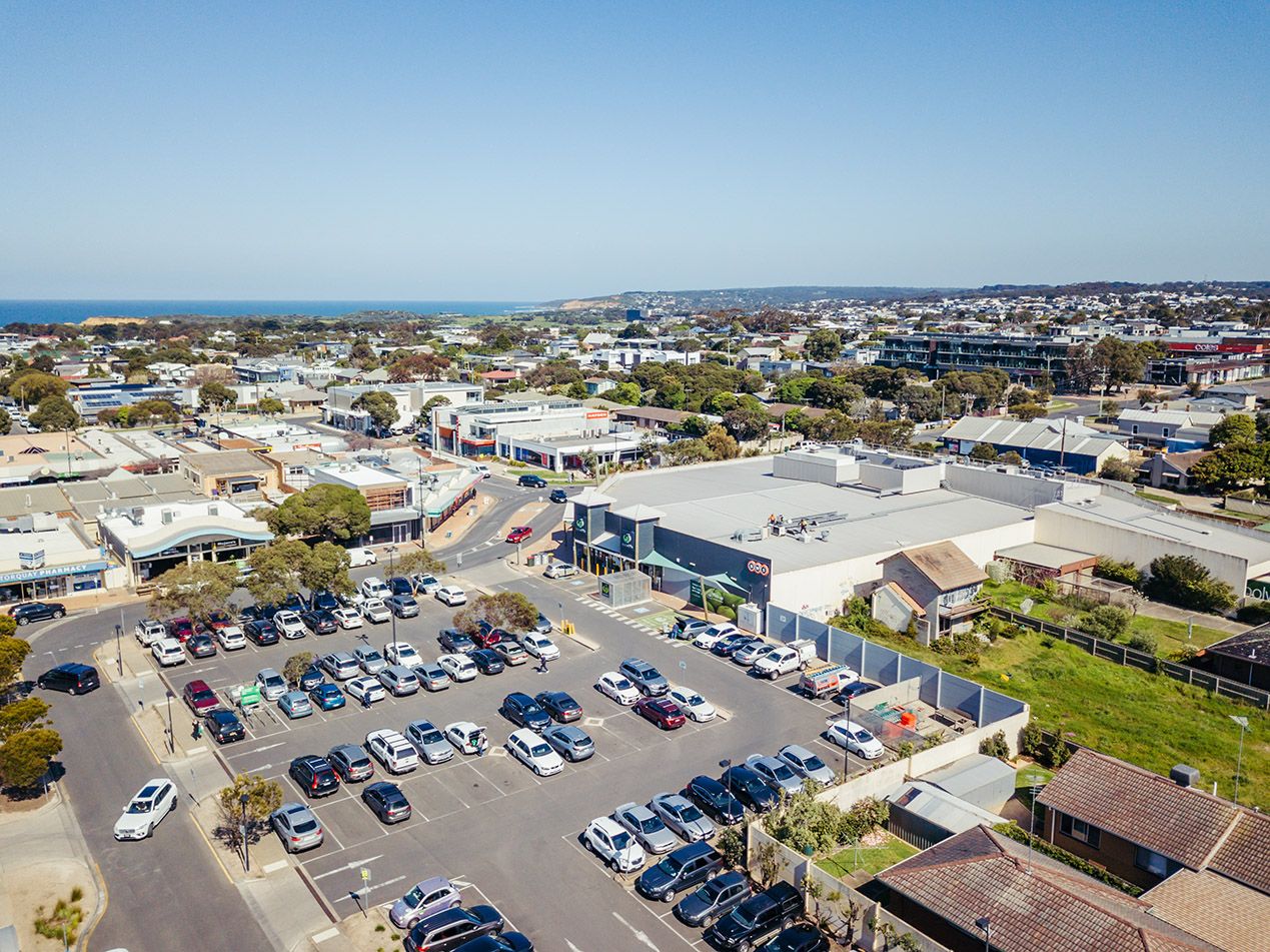 Aerial view of a large commercial parking lot with numerous vehicles and retail buildings.