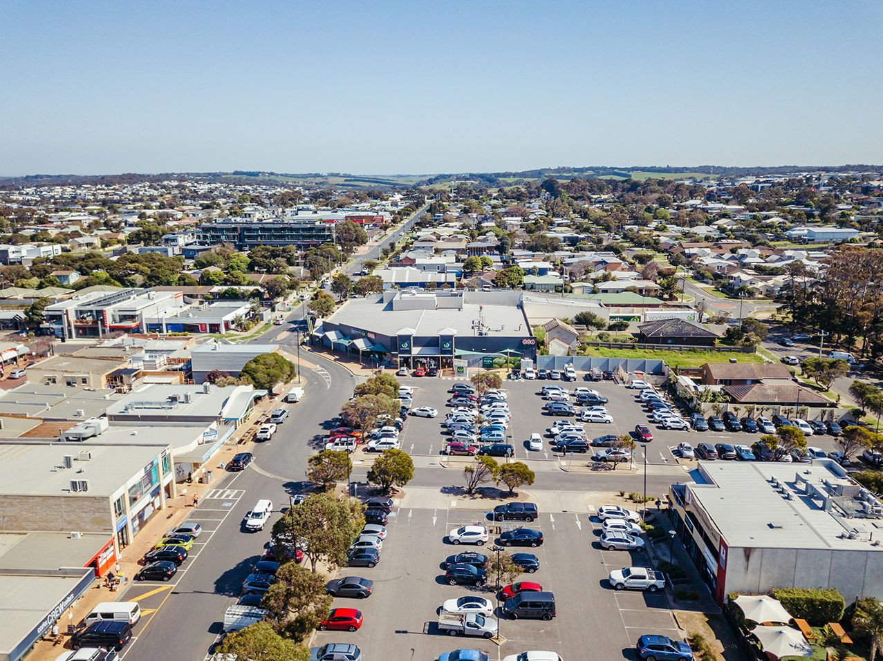 Bird's eye view of an expansive retail complex with parking lots and surrounding urban development.