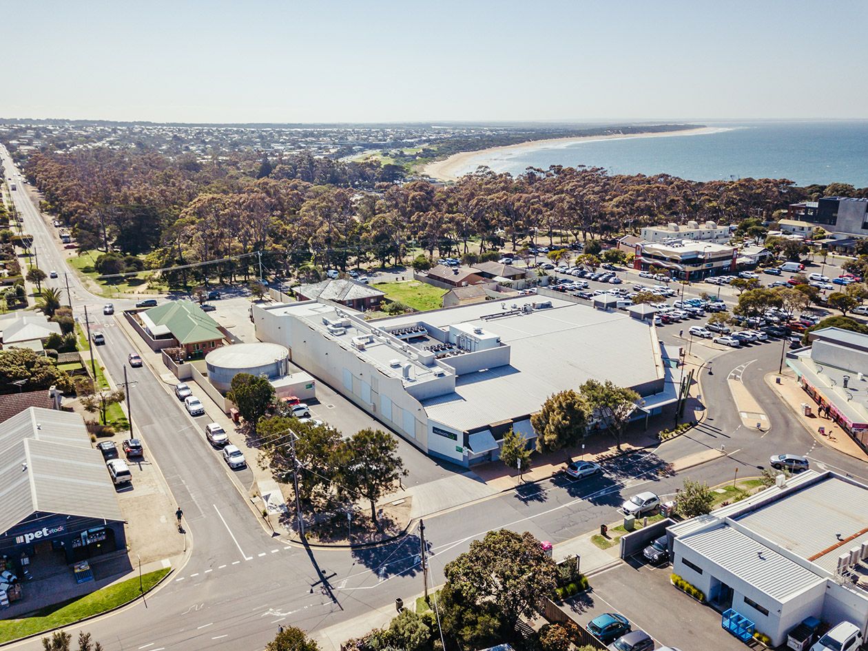 Drone shot of coastal retail center with white buildings and parking area near beach.