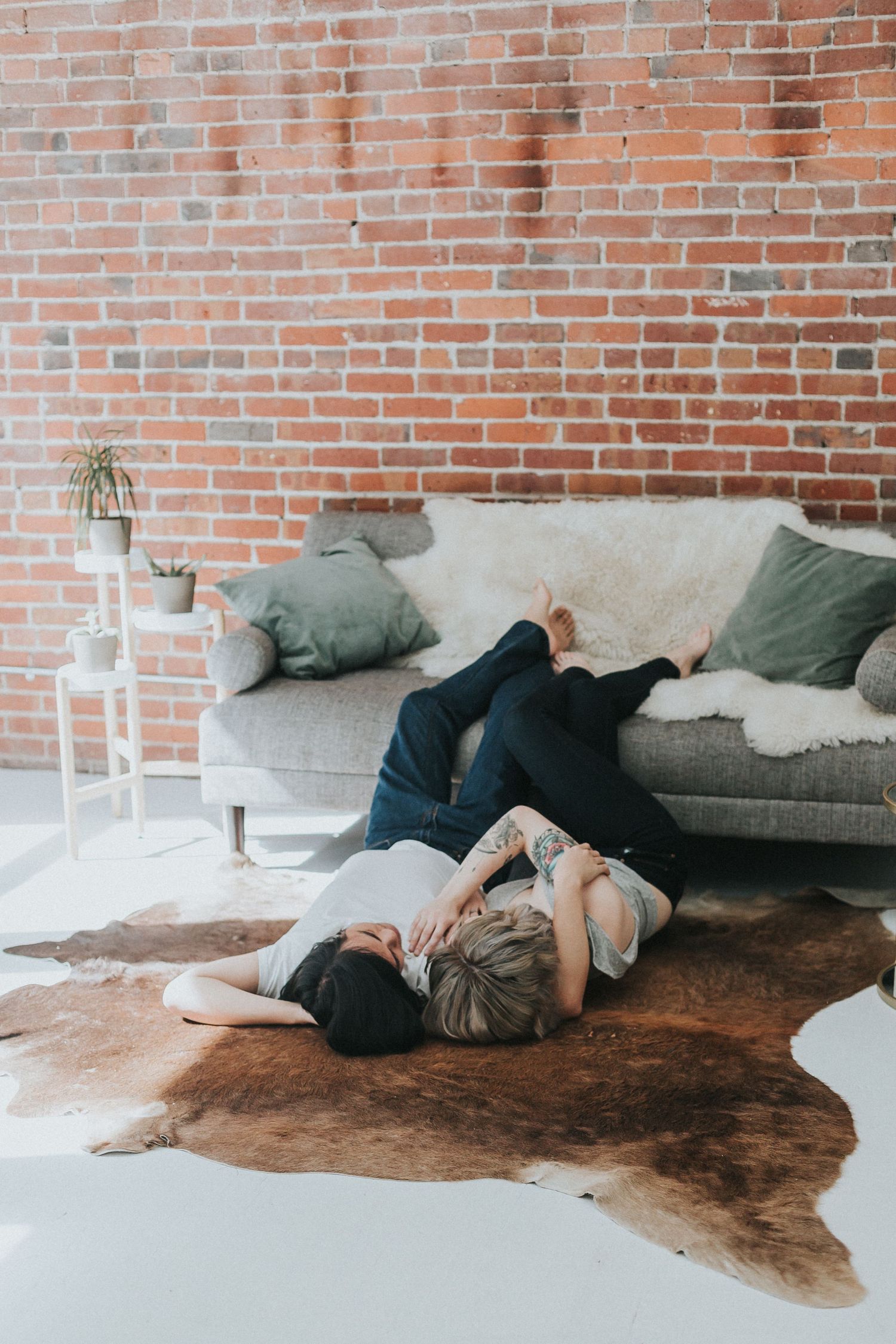 Artistic engagement photos on a cowhide rug against exposed brick walls.