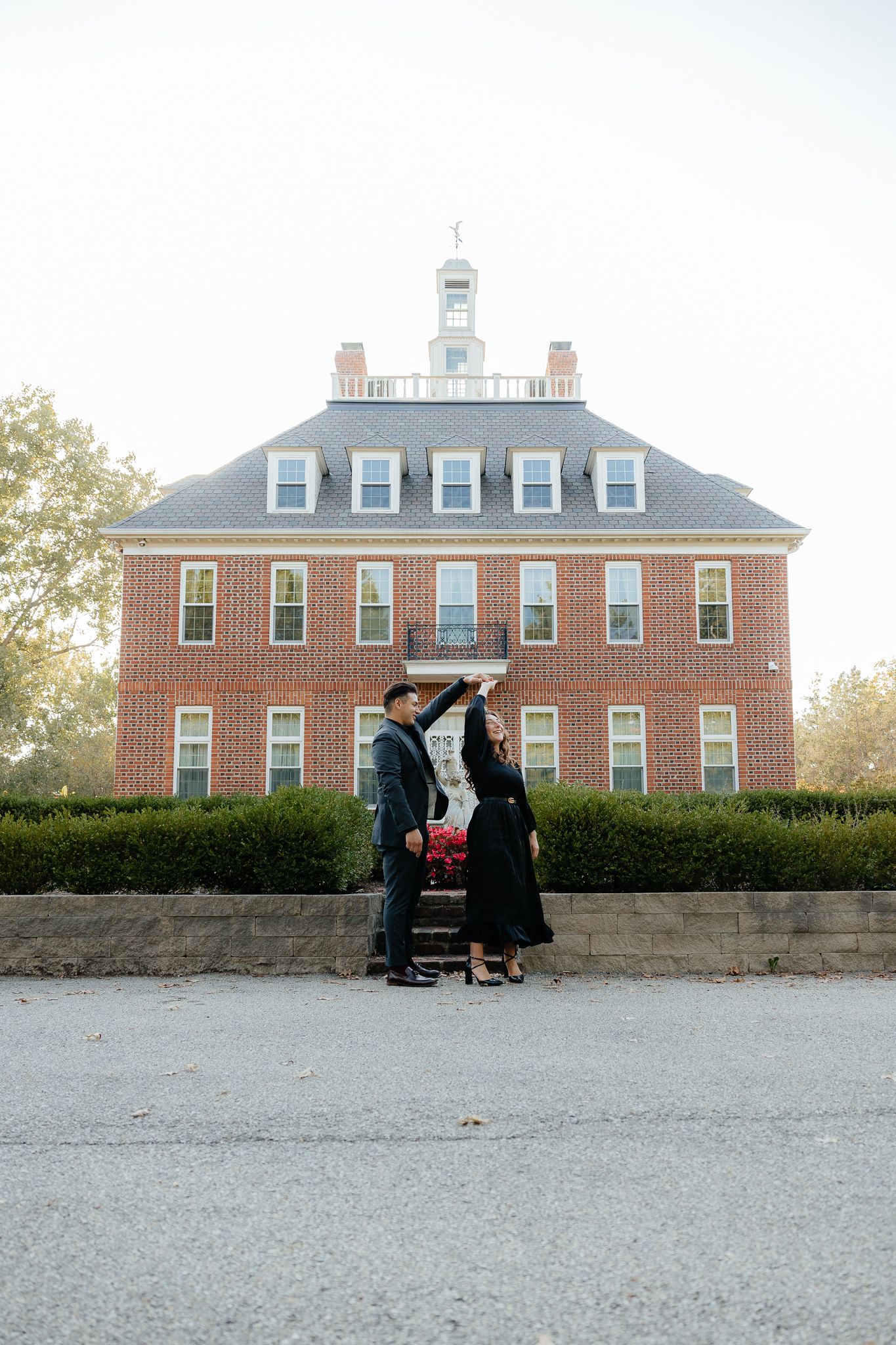 Romantic scene in front of historic brick mansion with couple posing on stone wall.