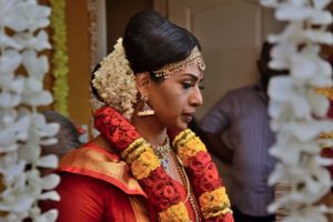 A woman in traditional South Indian bridal attire with flower garlands and gold jewelry.
