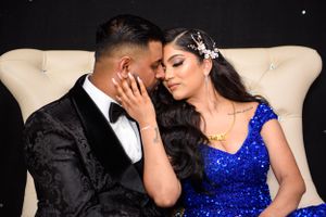 Intimate moment between couple in formal wear on cream sofa with sparkly backdrop.