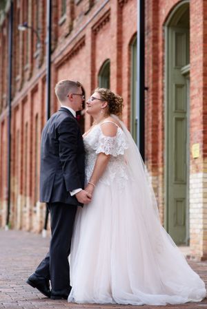 Wedding couple sharing intimate moment against brick building exterior.
