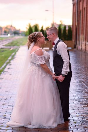 A romantic wedding couple posing on wet cobblestone streets, with the bride wearing a full white gown with lace details.