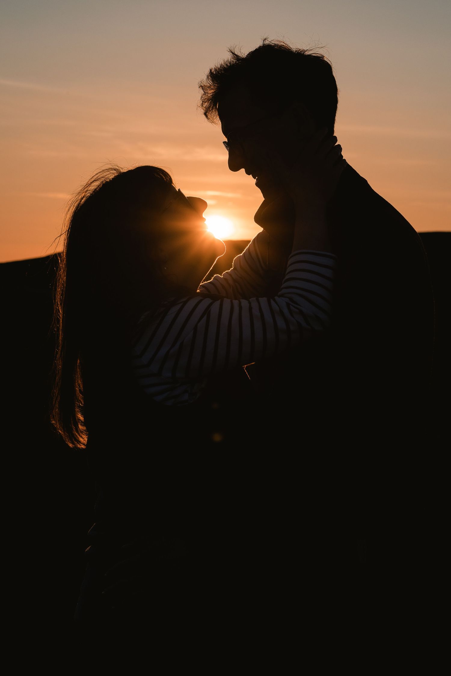 A young couple at golden hour. Their silhouette looking at each other, the sun is shining through the gap of their heads.