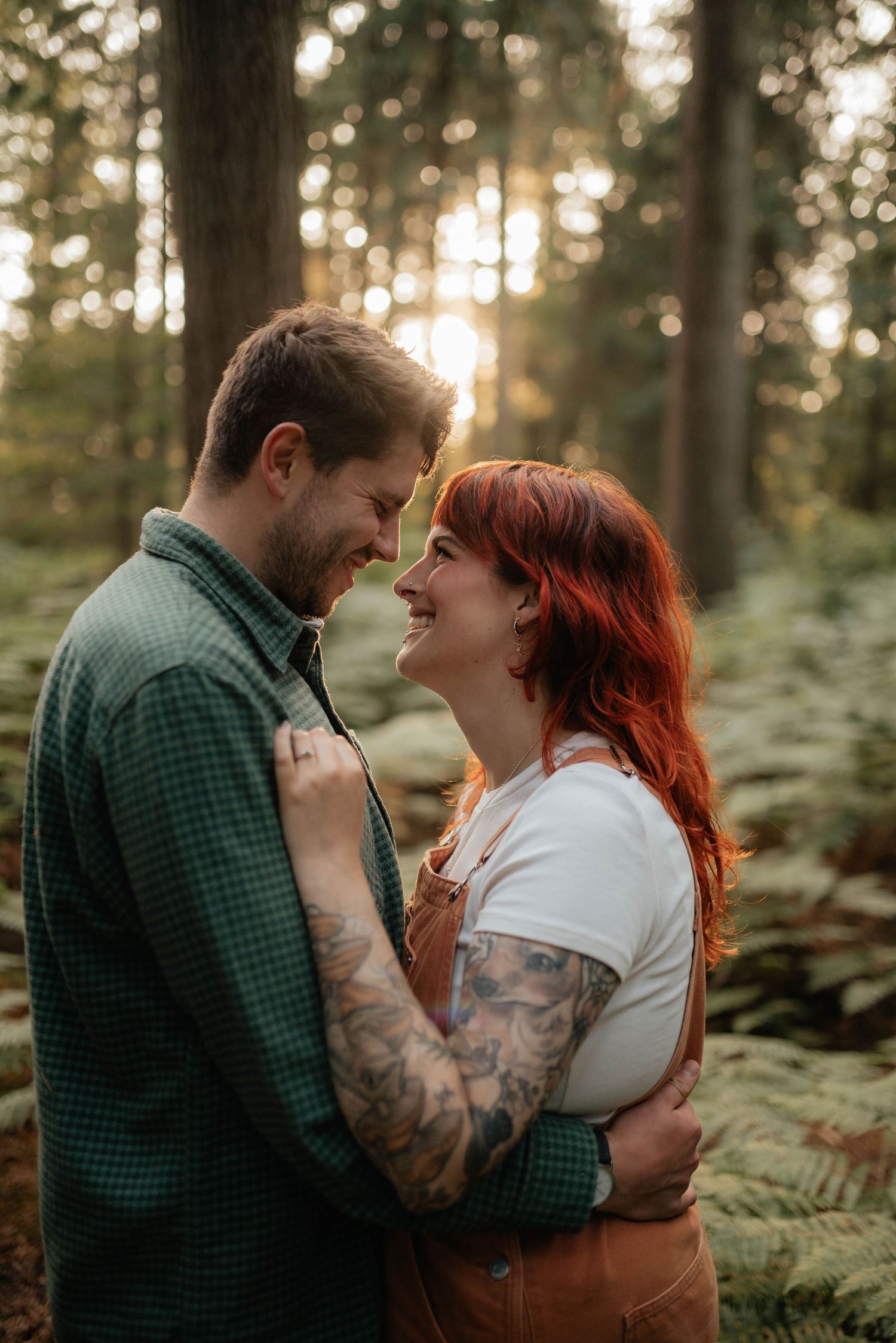A romantic couple embraces among ferns in a sunlit forest setting.