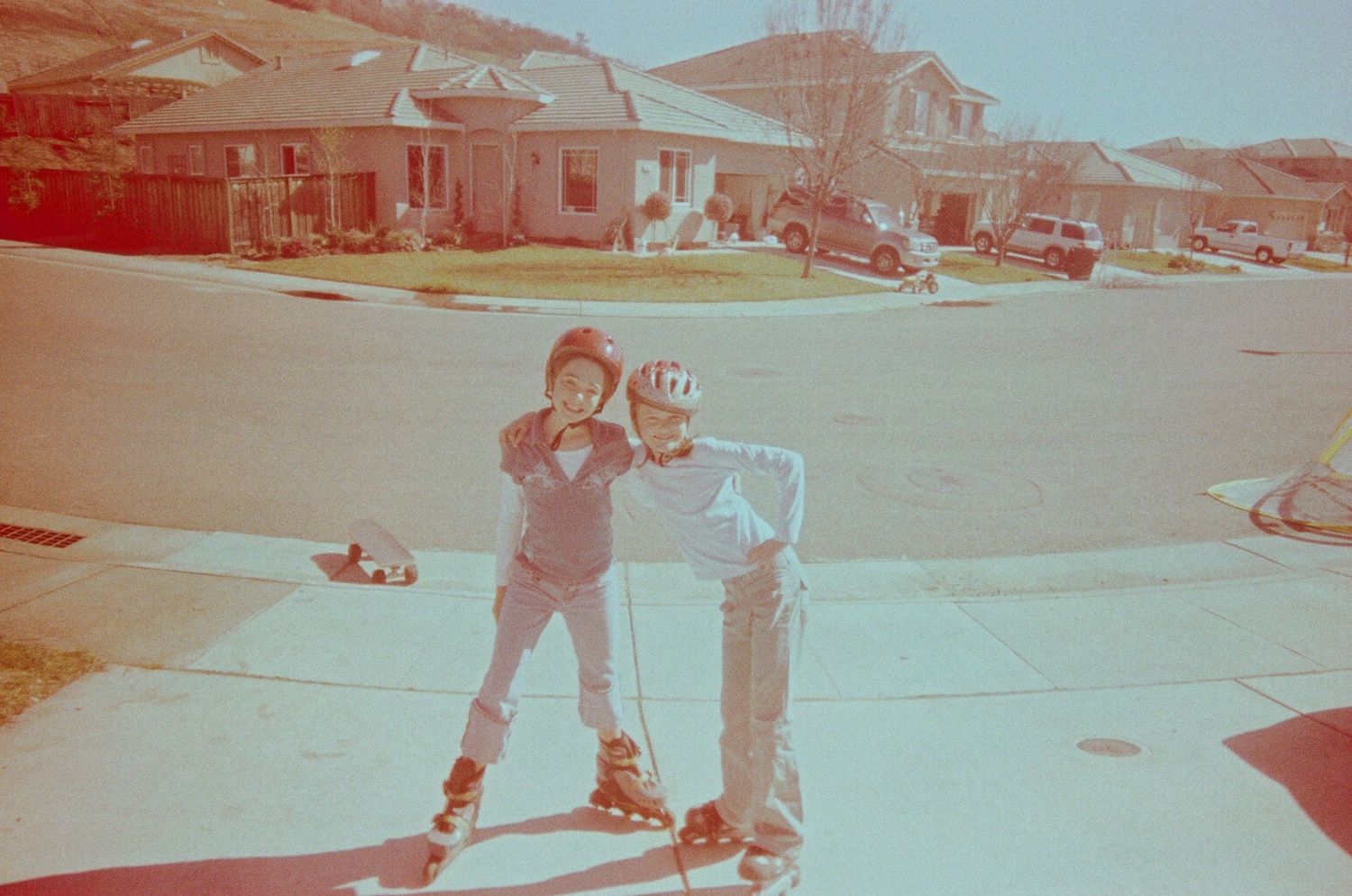 A vintage photograph of two kids posing on rollerblades in a suburban neighborhood.