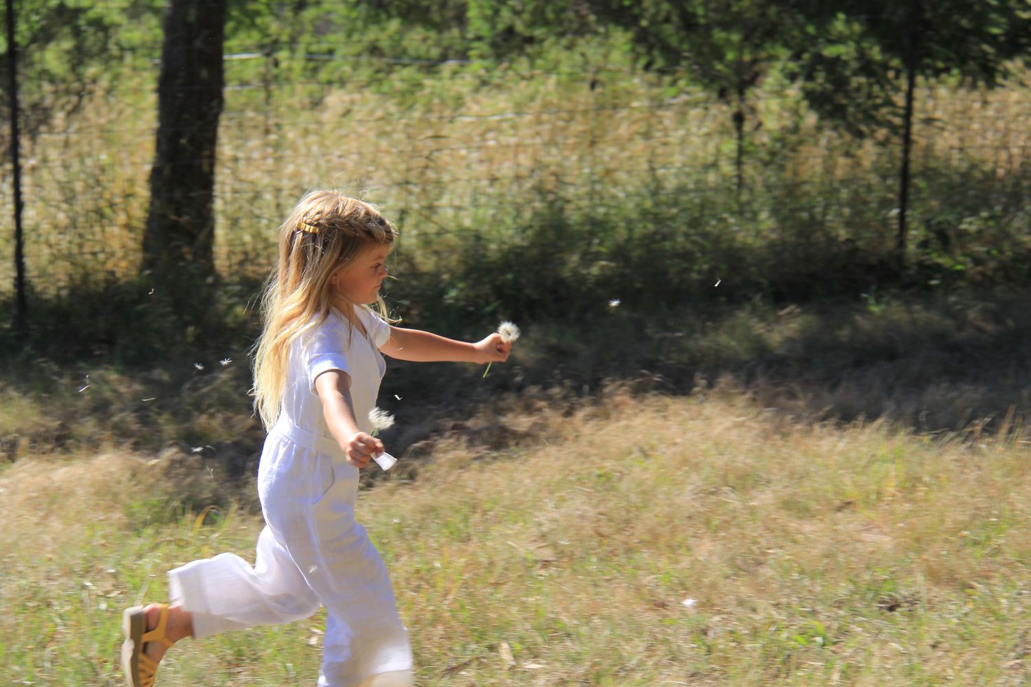 Someone wearing white runs joyfully through a sunlit meadow on a summer day.