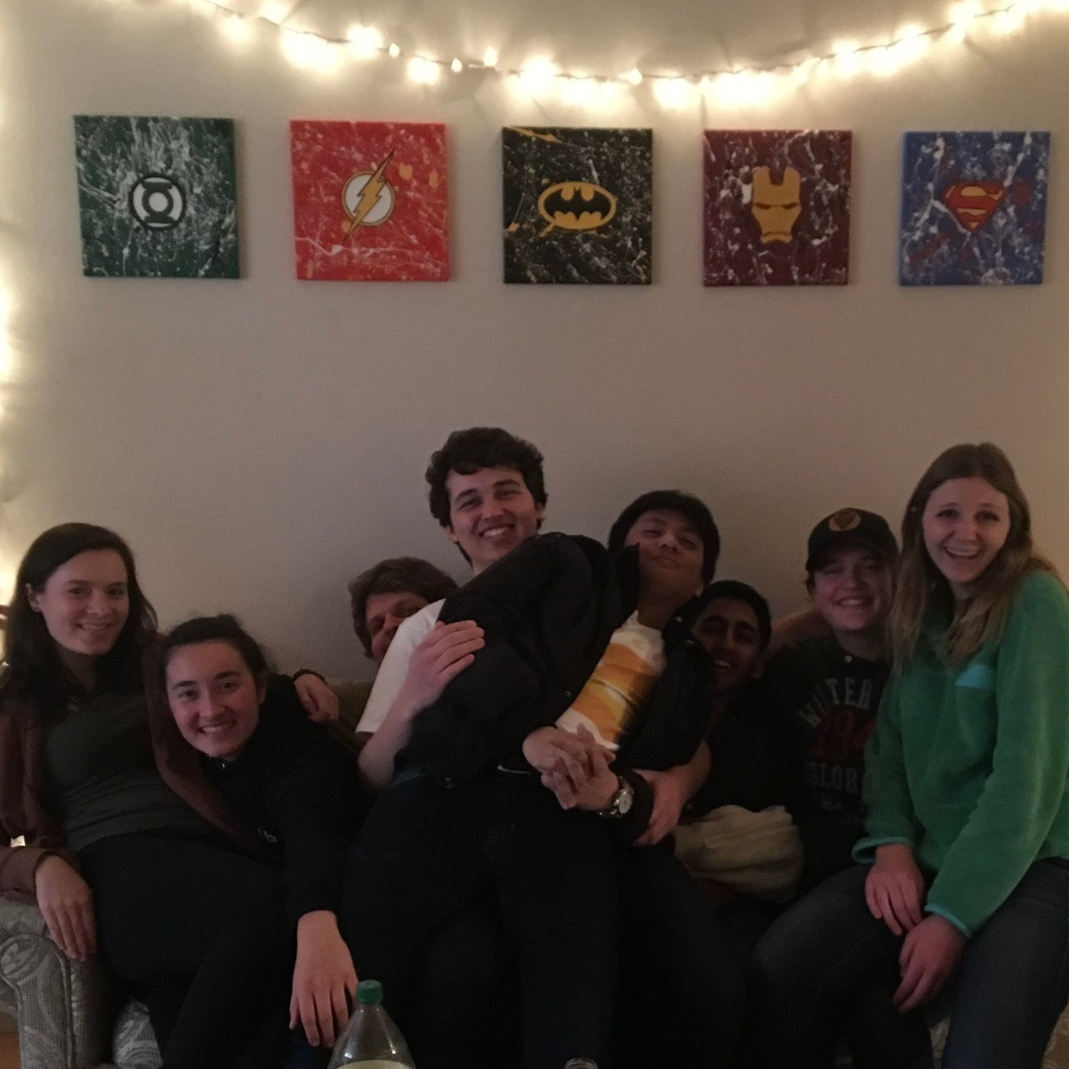 A group gathers under string lights and superhero wall art for a casual party.
