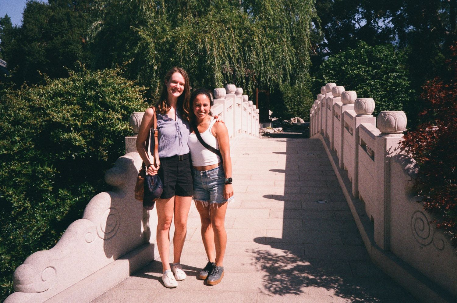 Two friends pose together on a bridge walkway on a sunny summer day.