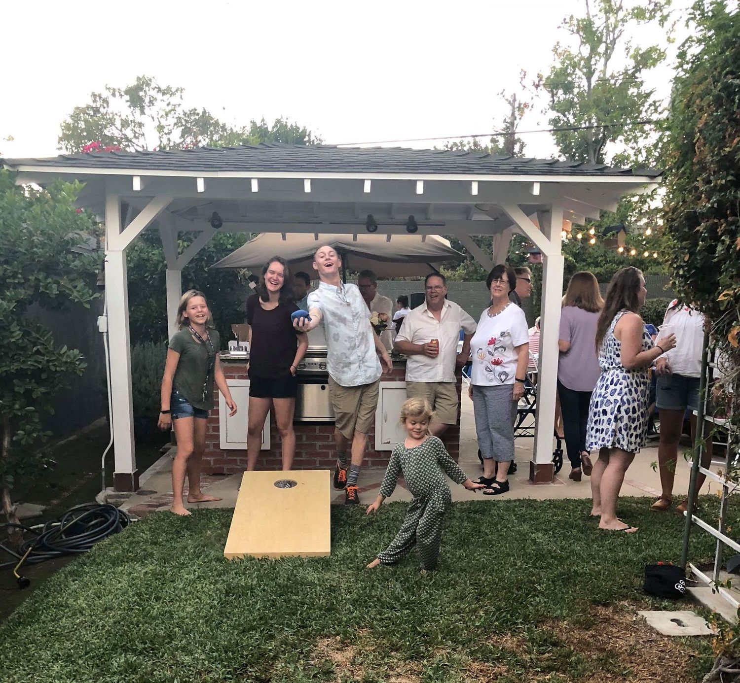 People gathered under a white pergola for an outdoor backyard party.