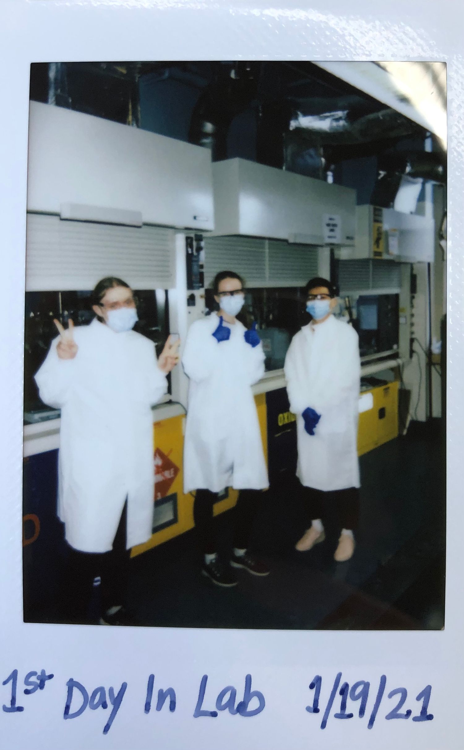 Three people in white lab coats and masks stand together on their first day in the laboratory.