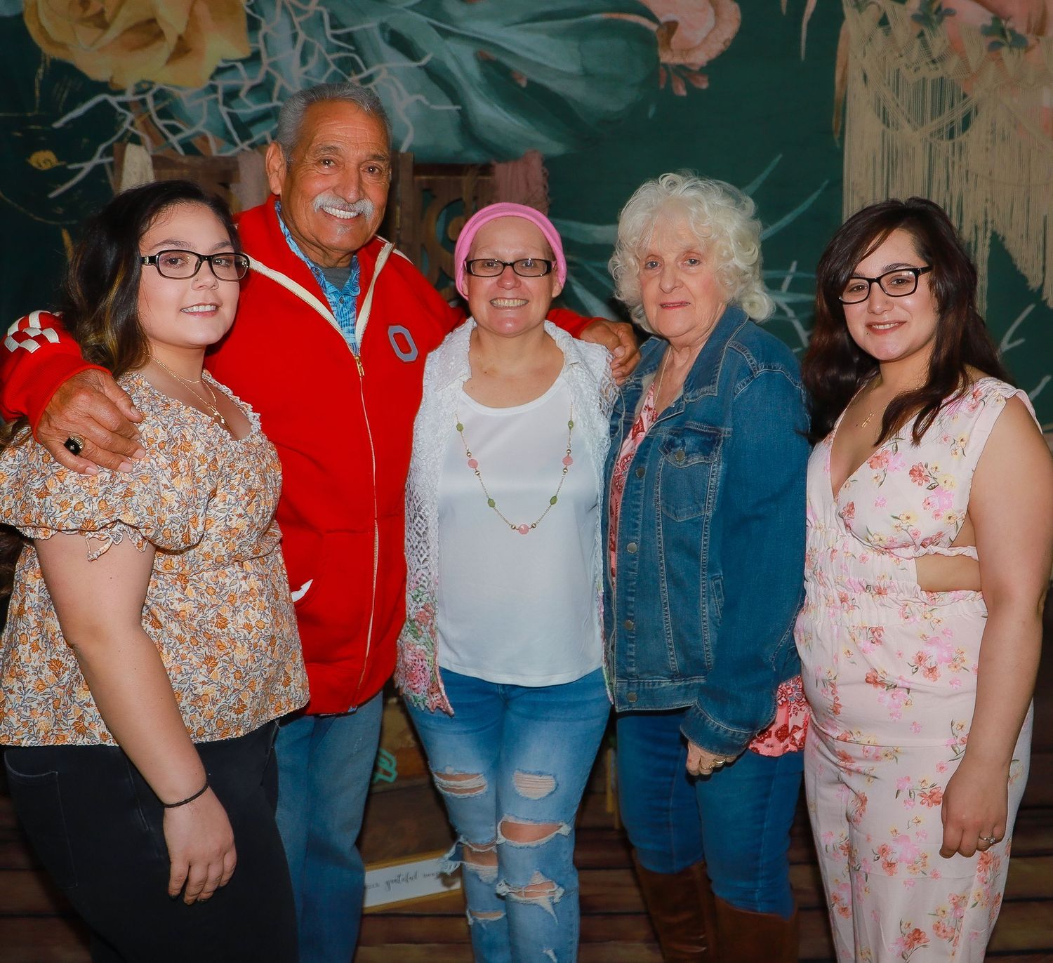 Casual group photo with mix of denim and floral outfits against decorated backdrop.