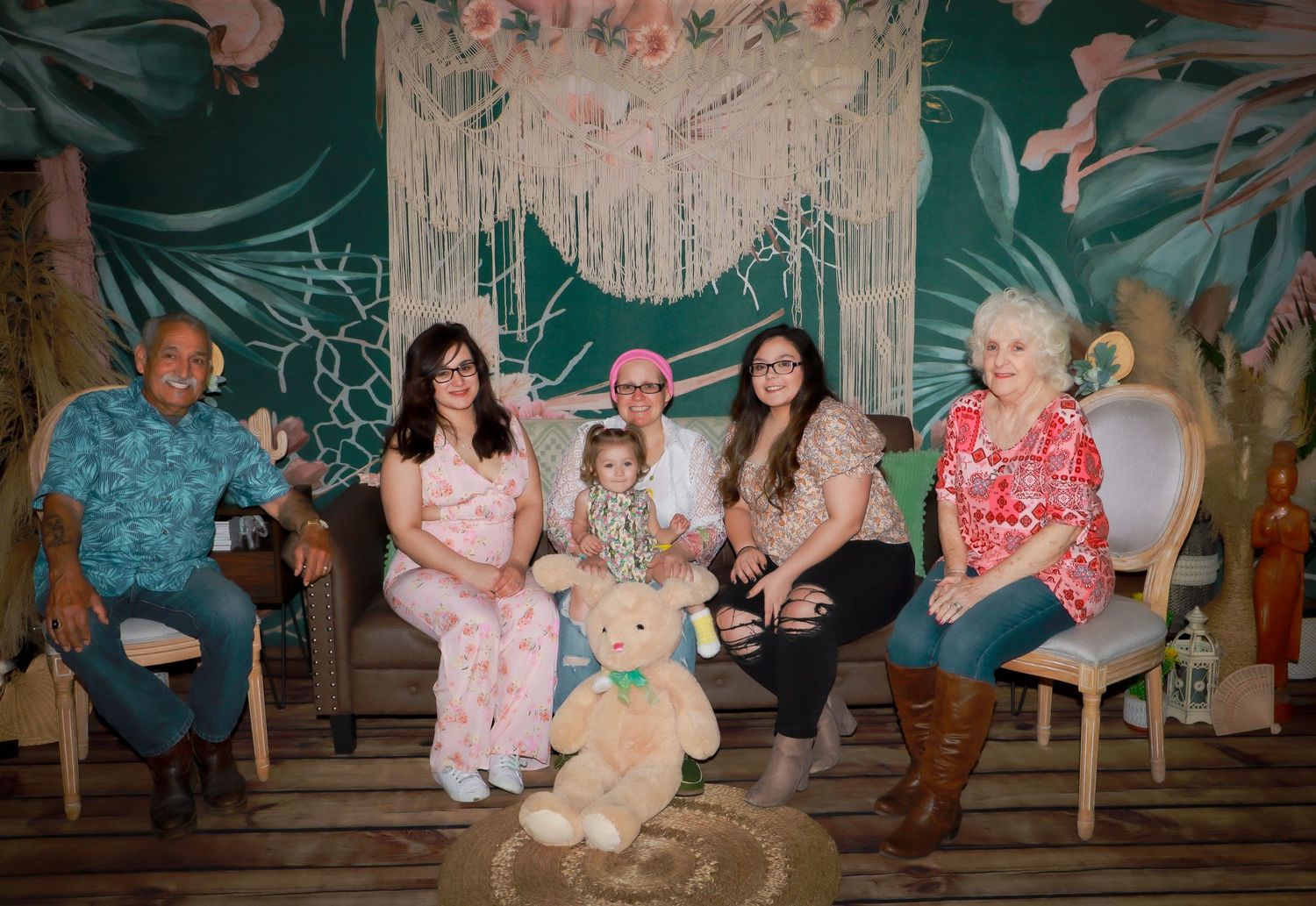 Group photo with stuffed bear in tropical themed setting with macrame wall hanging.