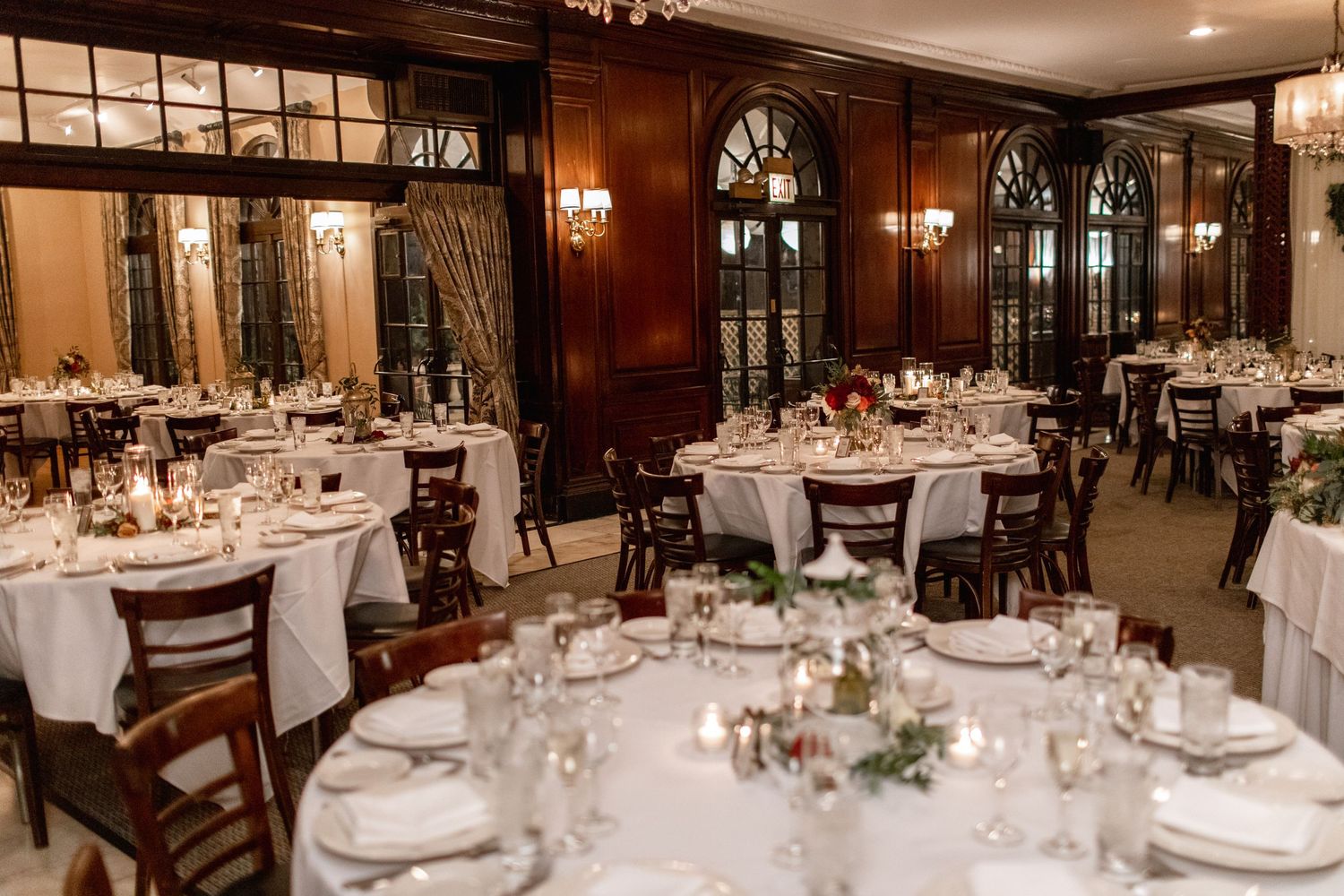 An elegant wedding reception venue with dark wood paneling and white tablecloths set for dinner.