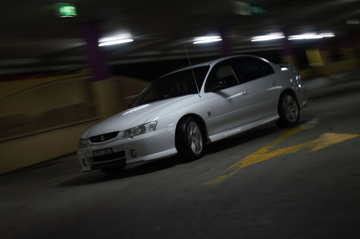 Silver sports sedan photographed in motion inside dimly lit parking garage.