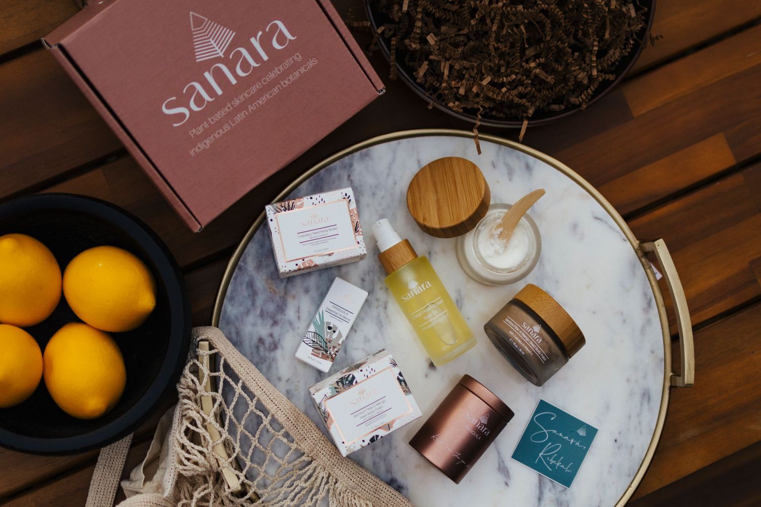 Flatlay of Sahara branded beauty products with lemons and wooden accents on tray.