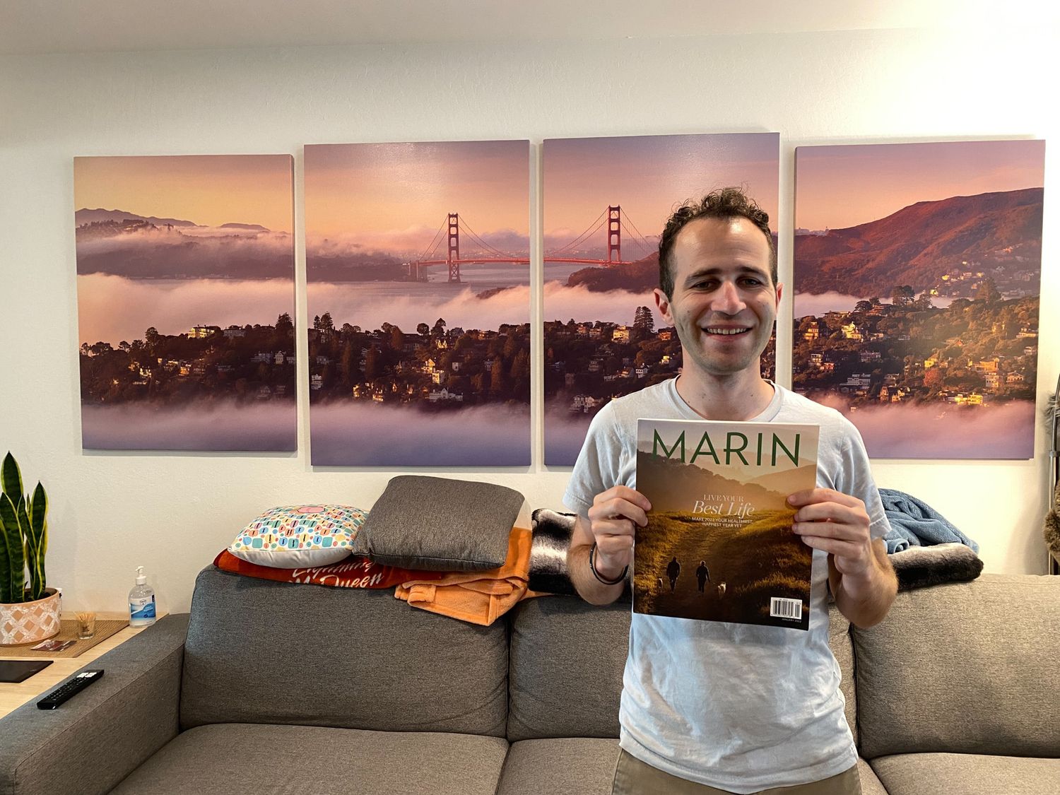 Traveler holds a Marin magazine in front of multi-panel wall art featuring the Golden Gate Bridge at sunset.